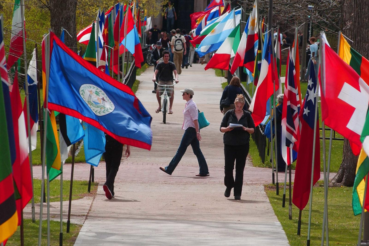 Various flags raised along sidewalk path, people walking