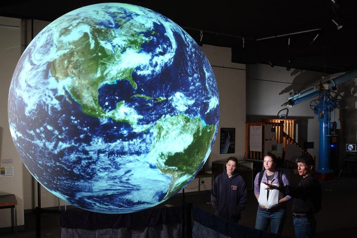 A virtual image of planet Earth with three figures looking at it