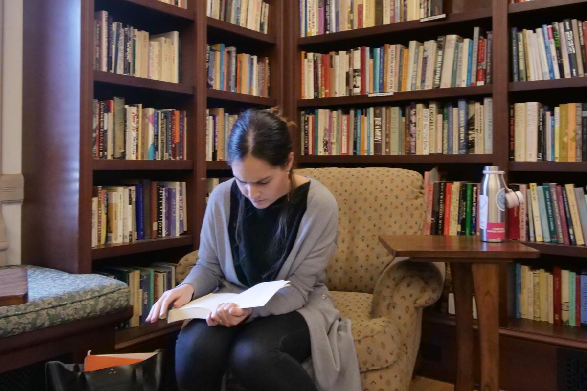 A student sits in a library room reading surrounded by books