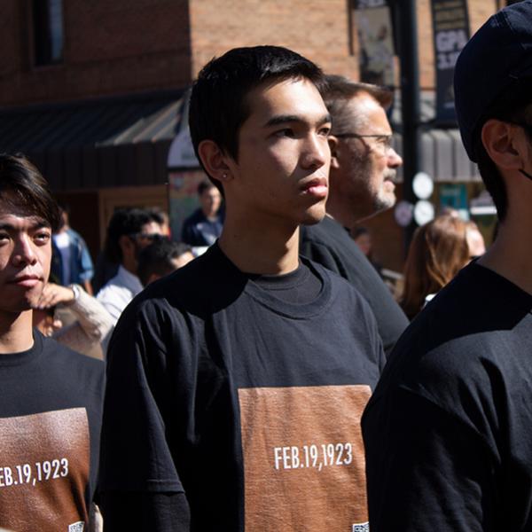 Close up image from political art performance in the form of a silent procession through downtown Boulder that took place in October 2022. A man is shown wearing a shirt with the date "February 19, 1923", which signifies the U.S. Supreme Court issued a ruling legally barring all Indians from becoming U.S. citizens and revoking citizenship from many who had attained it.