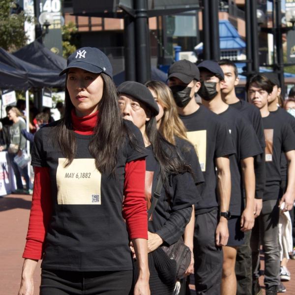 Asian Americans walk in a political art action to stop asian hate. Participants have a date on their shirt to signify a date of supreme court landmark cases targeting Asians in America. May 6, 1882 is visible on first participant's shirt.