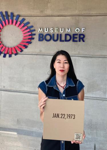 Angie Eng, artist, shown holding one of the wooden plaques in front of the Museum of Boulder. The date shown on plaque is January 22, 1973. This date signifies the supreme court case Roe V Wade