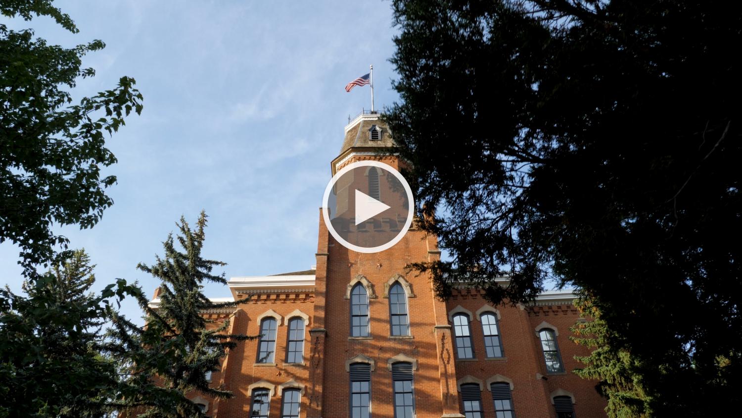 Image of Old Main surrounded by trees with a video play button