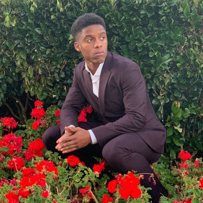 Nadir Shakir in a suit kneeling near some red flowers