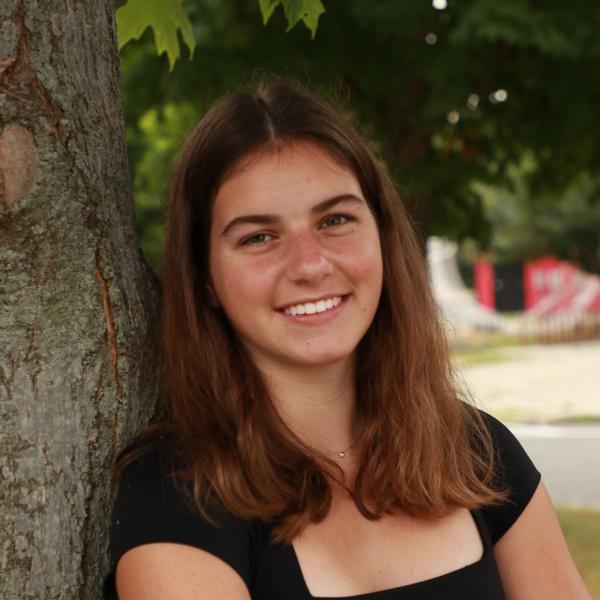 Cate Trautman leans against a tree with her arms folded