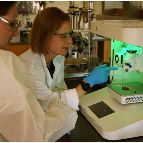 Photo caption: Morgan Riffe (left), a PhD candidate in Materials Science & Engineering, looks on while Meg Cooke, PhD, research associate in the BioFrontiers Institute, explains the 3D printing process to fabricate biomaterial scaffolds.