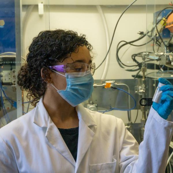 Megan English in lab wearing eye protection, mask, and gloves while holding lab sample