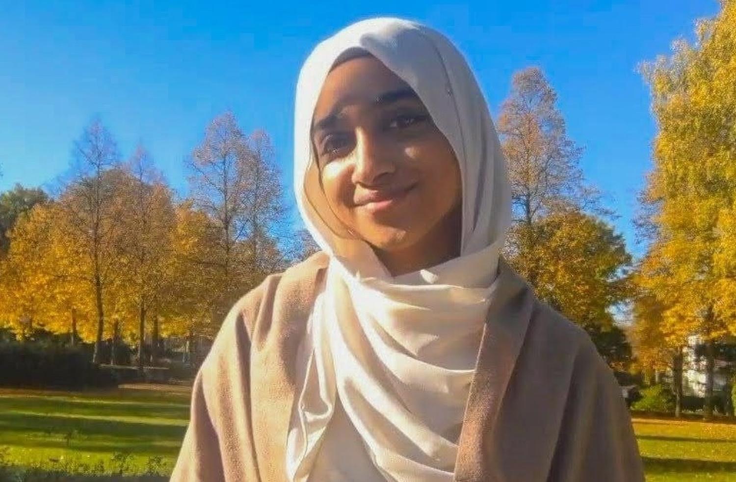 Nafeesah Ibrahim with a head covering and trees with fall colors in the background