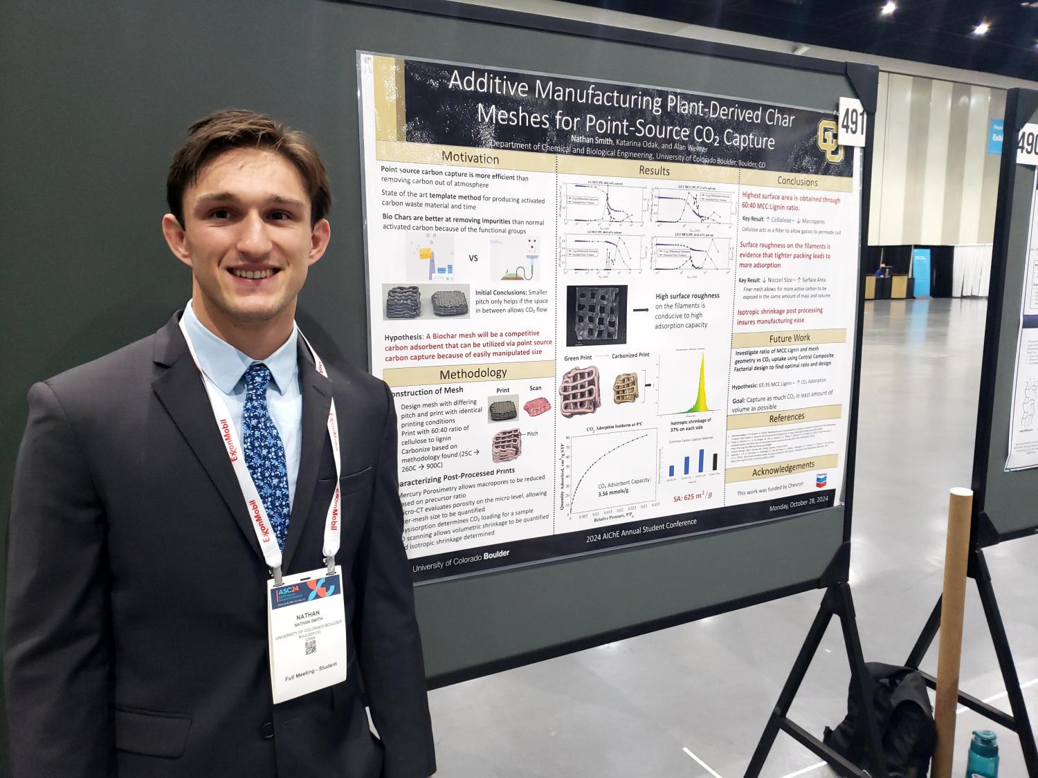 Nathan Smith in a suit and wearing a conference badge, stands by his poster.