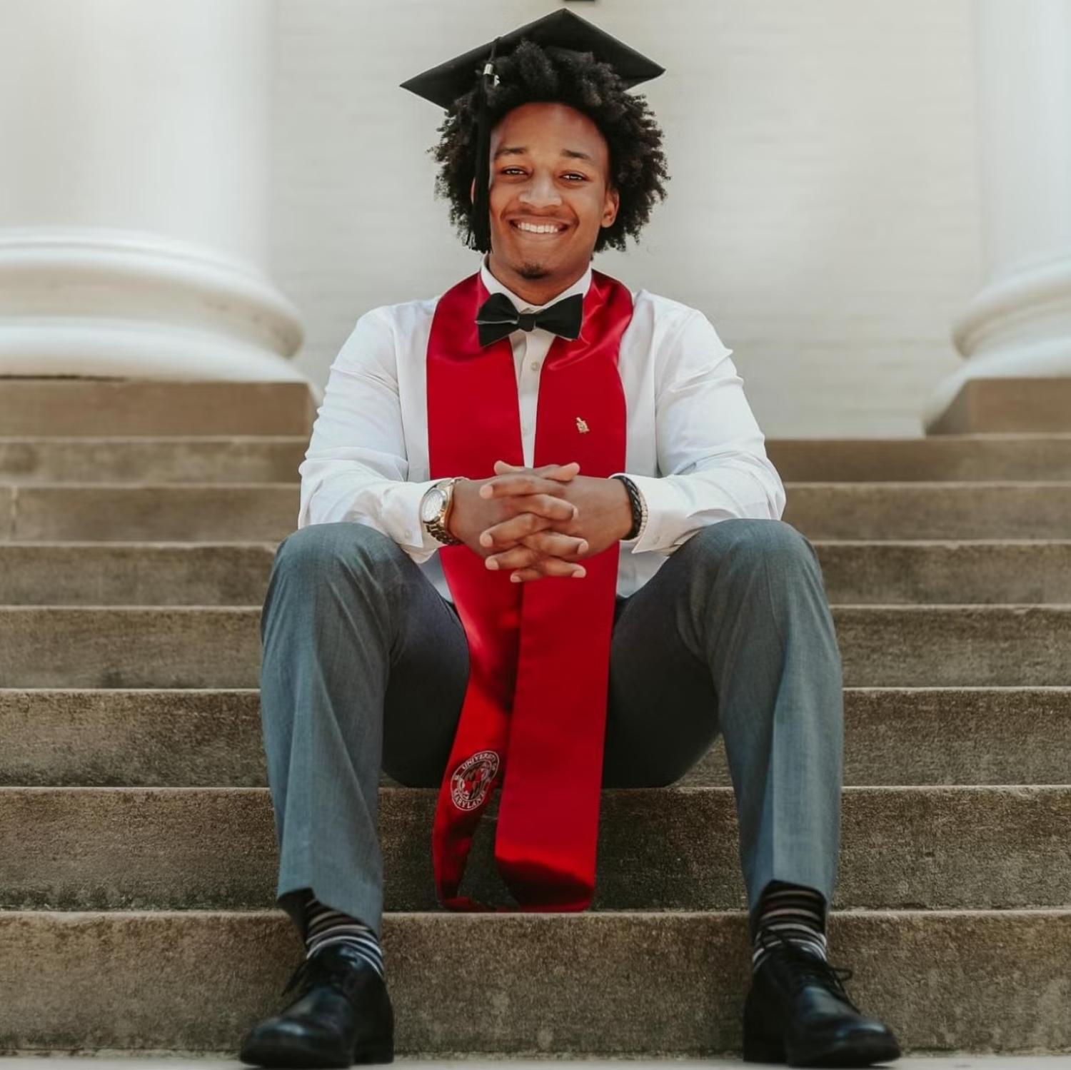 Brandon Oliphant sitting on some concrete steps, dressed in a graduation hat and scarf and a white shirt and bow tie.