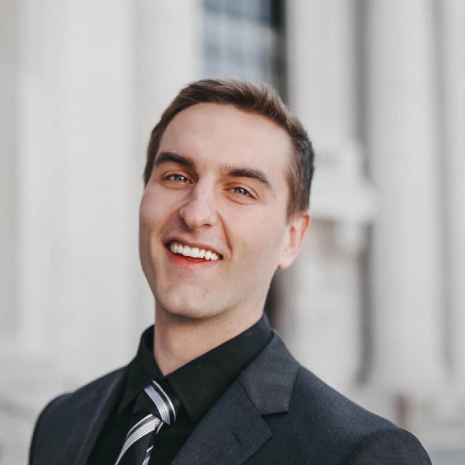 Cody Ritt in a dark suit and tie with a building blurred in the background