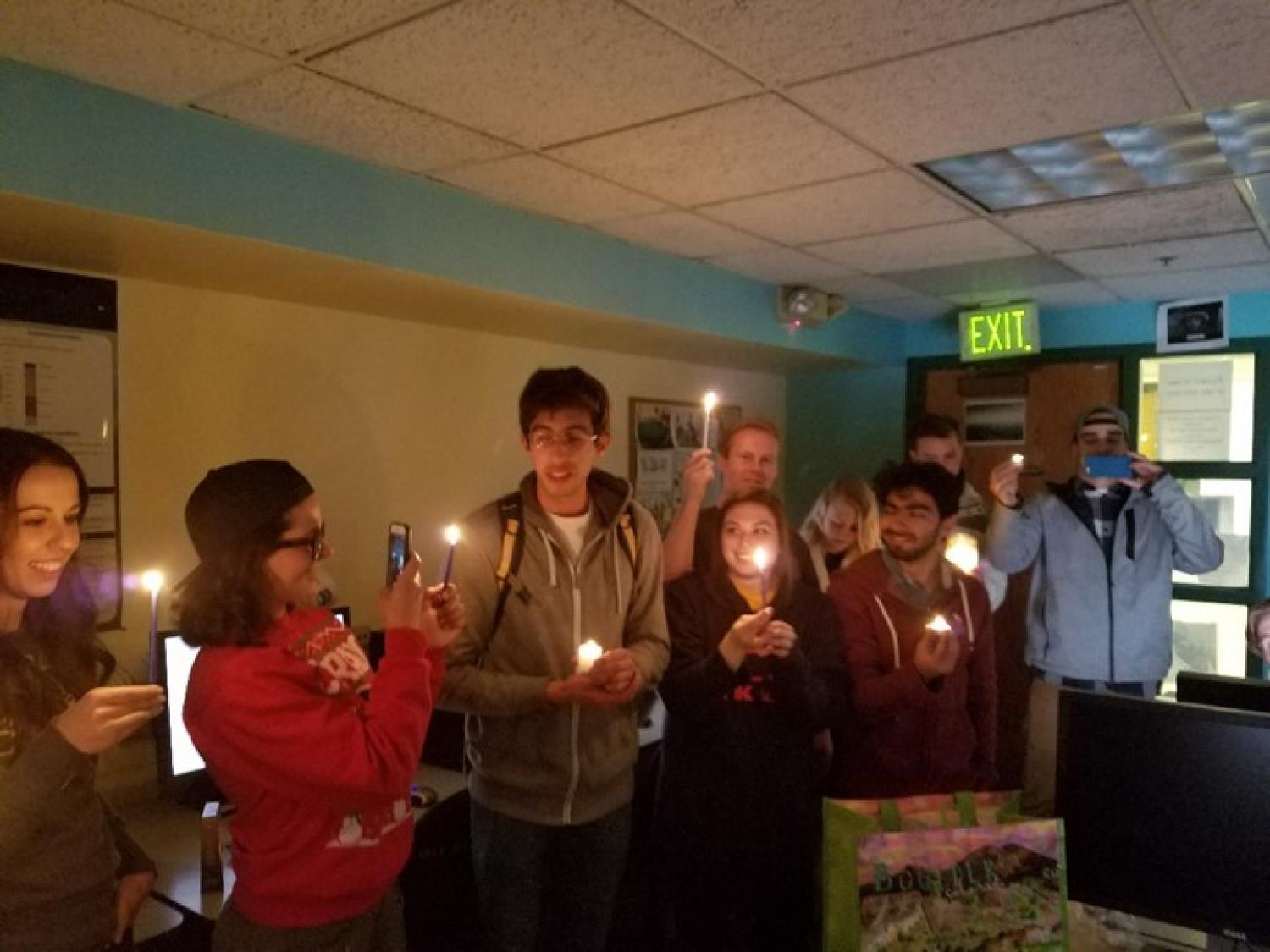 Students hold candles in a dark computer lab