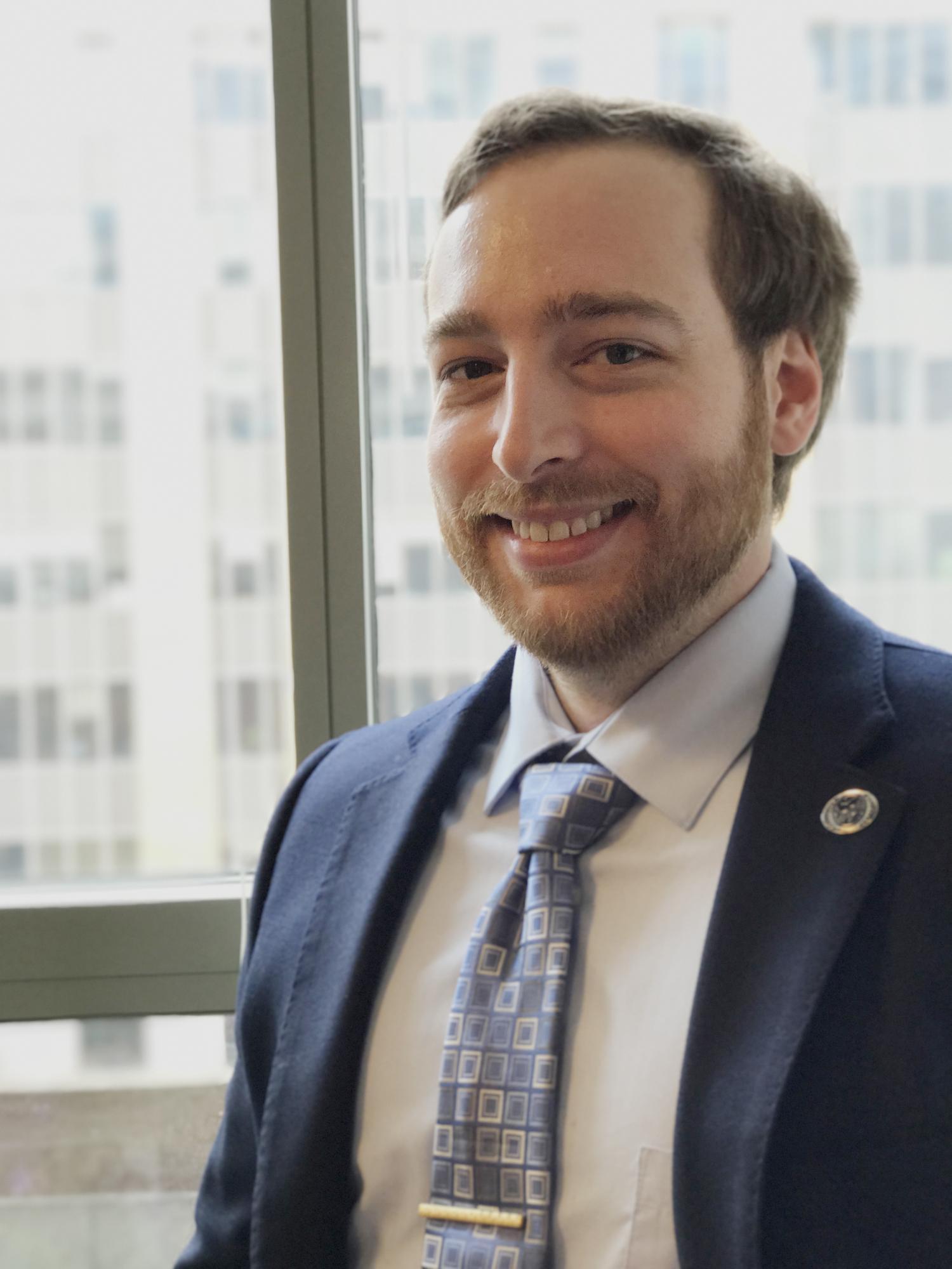Sam Goodman in suit in front of windows