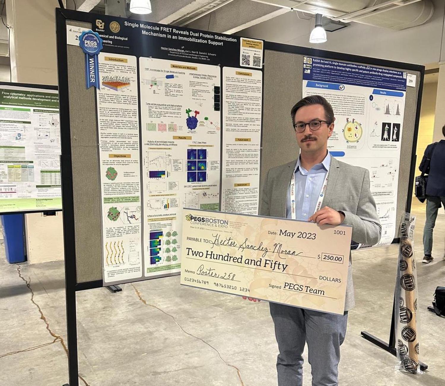 Hector Sanchez-Moran holding a very large check for $250, showing he won the poster prize.