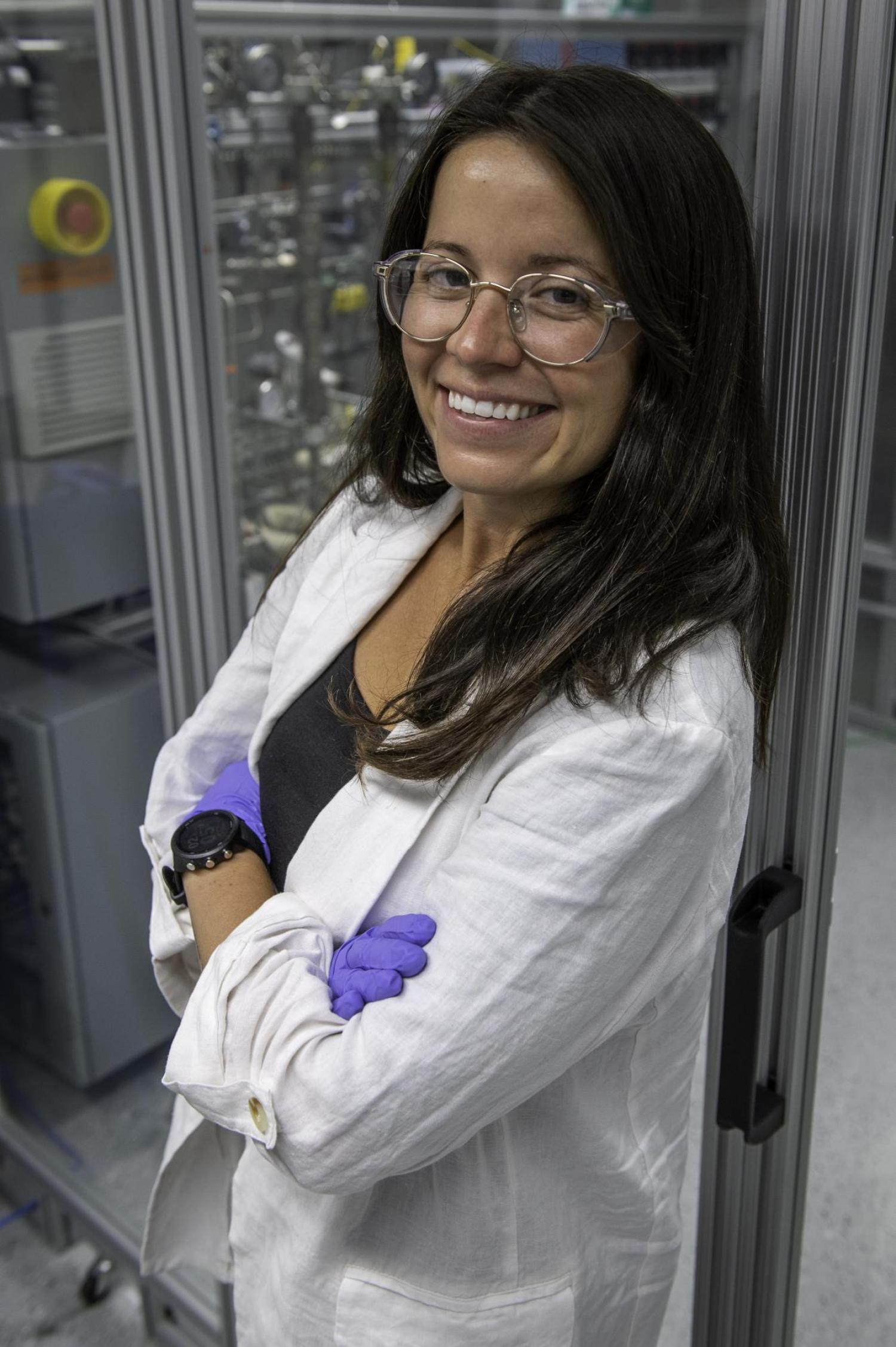 Katrina Knauer stands in a lab coat and is wearing plastic gloves