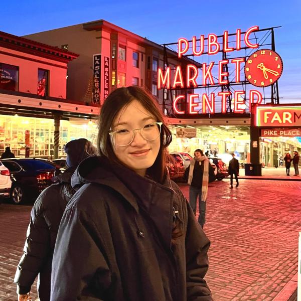 Krista Phommatha at night in front of a neon sign that says "Public Market Center."