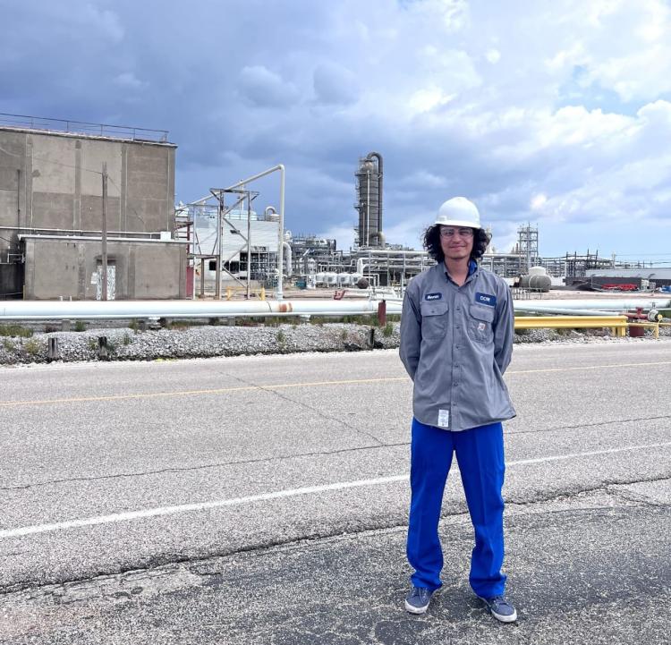 Barrientos in a hard hat in front of an industrial area and cloudy skies.