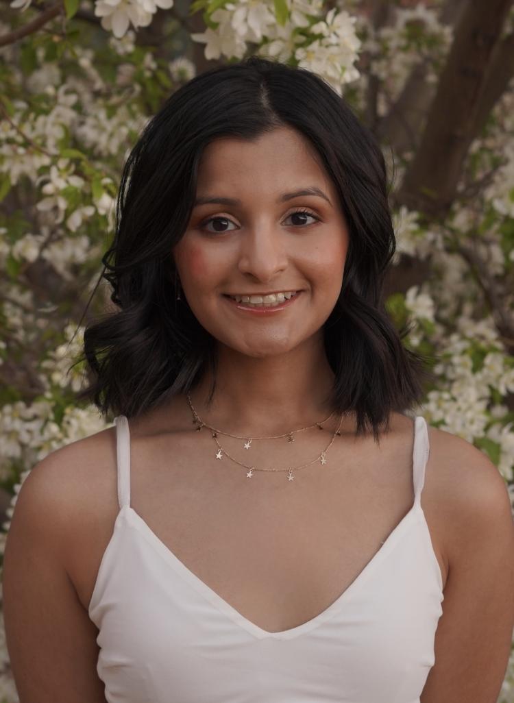 Tanvi Patil in a white summer dress in front of a flowering tree.