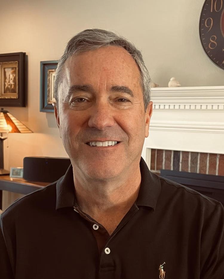 Bart Carpenter with the top of a fireplace and some framed pictures in the background