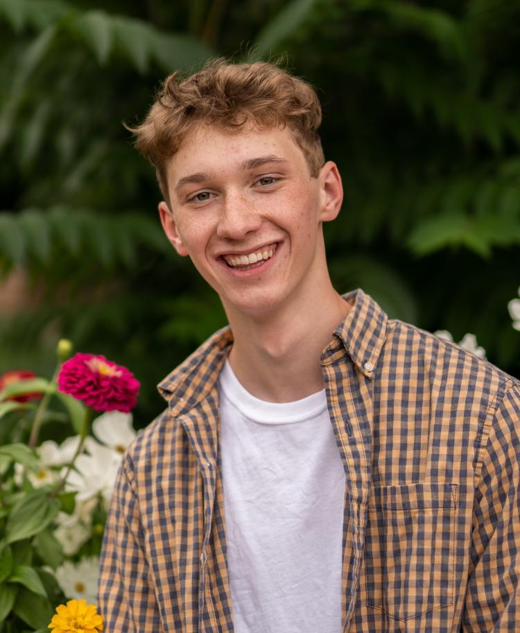 Jackson Carter in an open button-down shirt and a t-shirt underneath it. A faded palm tree is in the background