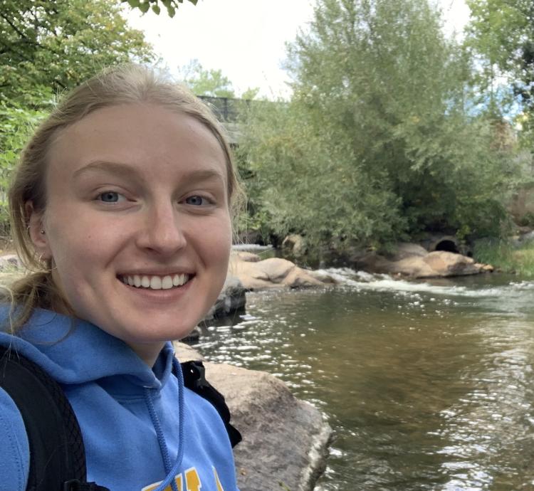 Mady Murphy in a hoodie sweatshirt by a stream.