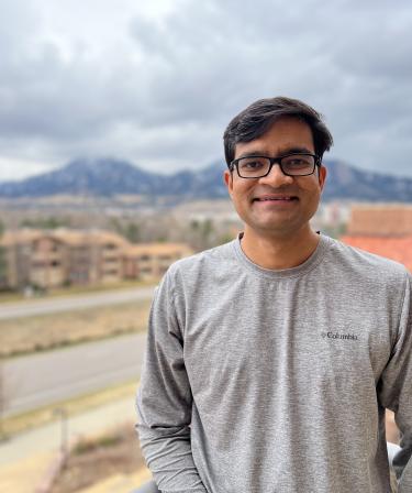 Kaustav Bera stands in a long-sleeve t-shirt with the mountains blurred in the background on a cloudy day.