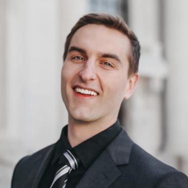Cody Ritt in a dark suit and tie with a building blurred in the background