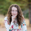 Arianna McCarty with her chin resting on her folded hand and blurred trees in the background.
