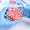 Meat in a petri dish held by a gloved hand in a lab