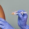 closeup of doctors hands holding a vaccine near someone's arm