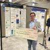 Hector Sanchez-Moran holding a very large check for $250, showing he won the poster prize.