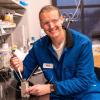 Todd Whittaker working at the bench in the lab with a blue jumpsuit on