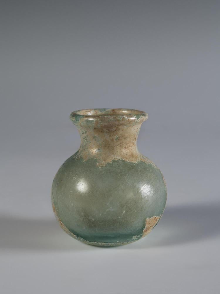 Photograph of clear glass vessel with rounded body and base and short neck that flares to a rounded mouth, from the side against a neutral gray background.