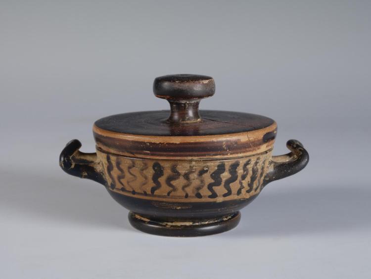 Photograph of a lidded lekanis, with lid in place, from the side against a neutral gray background.