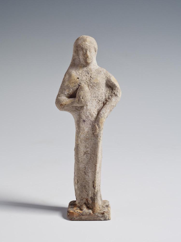 Photograph of a front-facing female figurine, holding a round object against chest, from the front against a neutral gray background.