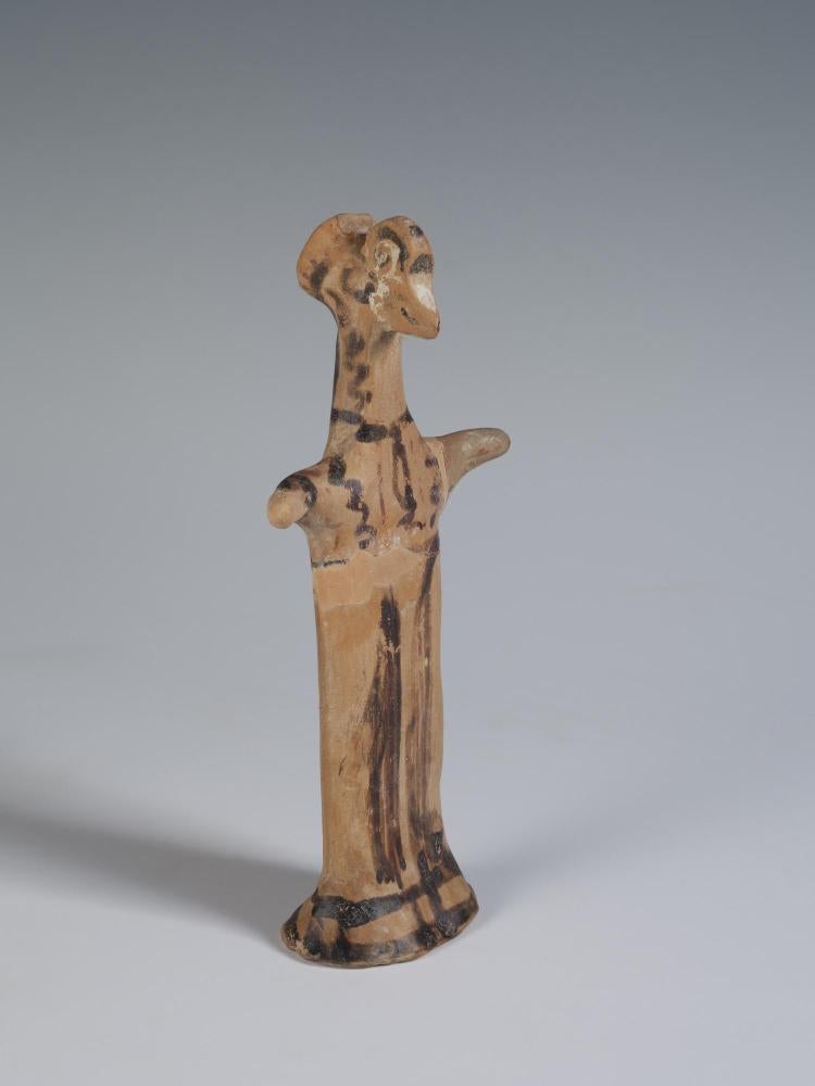 Photograph of terracotta female figurine, angled slightly to the viewer's right, against neutral gray-blue background.