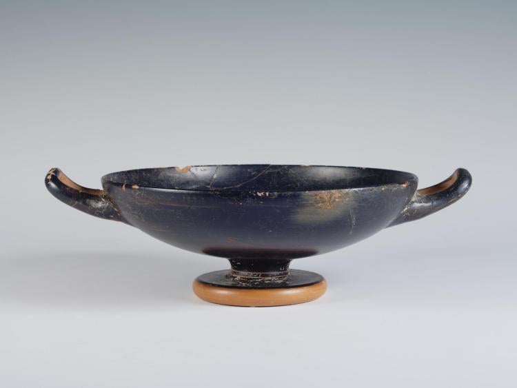 Photograph of a black-gloss kylix, from the side against a neutral gray background.