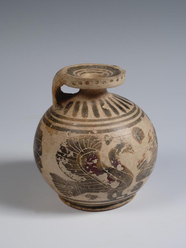Photograph of small, rounded aryballos, from the side, against a neutral gray background.