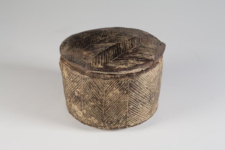 Photograph of a Minoan pyxis with its lid in place, from the side against a neutral gray background.