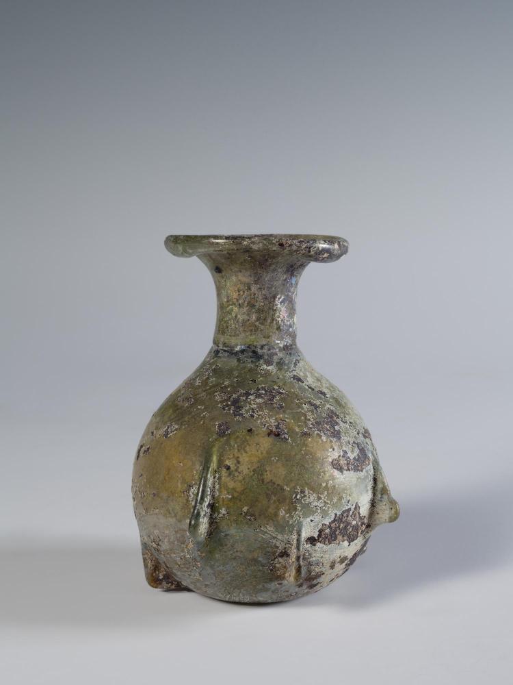 Photograph of a glass vessel with a round body and relatively short neck that flares into a horizontal, disk-shaped mouth, from the side against a neutral gray background.