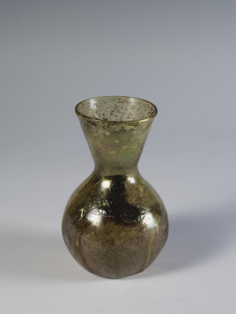 Photograph of glass vase, with flat bottom, rounded body, and neck with straight sides that flare outward to mouth, from a slightly raised angle against a neutral gray background.