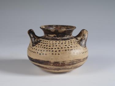 Photograph of squat jar, tan with brown slip decoration, from the side against a neutral gray background.