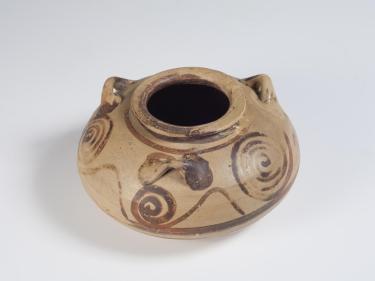 Photograph of squat jar, tan with brown slip decoration, from high angle against neutral gray background.