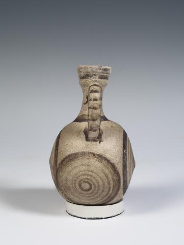 Photograph of a small, rounded jug from side, tan with brown decoration, against a neutral gray background.