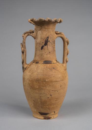 Photograph of yellowish-tan-colored amphora against neutral gray background.