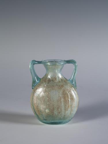 Photograph of a clear glass jar with a rounded body, two handles that connect the shoulders to the mouth, from the side against a neutral gray background.