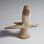 Photograph of terracotta harpy figurine, with a bird body and a human woman's neck and head, angled to viewer's right, against a neutral gray background