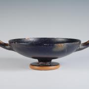 Photograph of a black-gloss kylix, from the side against a neutral gray background.