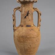 Photograph of yellowish-tan-colored amphora against neutral gray background.