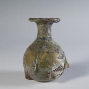 Photograph of a clear glass jar with a rounded body, two handles that connect the shoulders to the mouth, from the side against a neutral gray background.